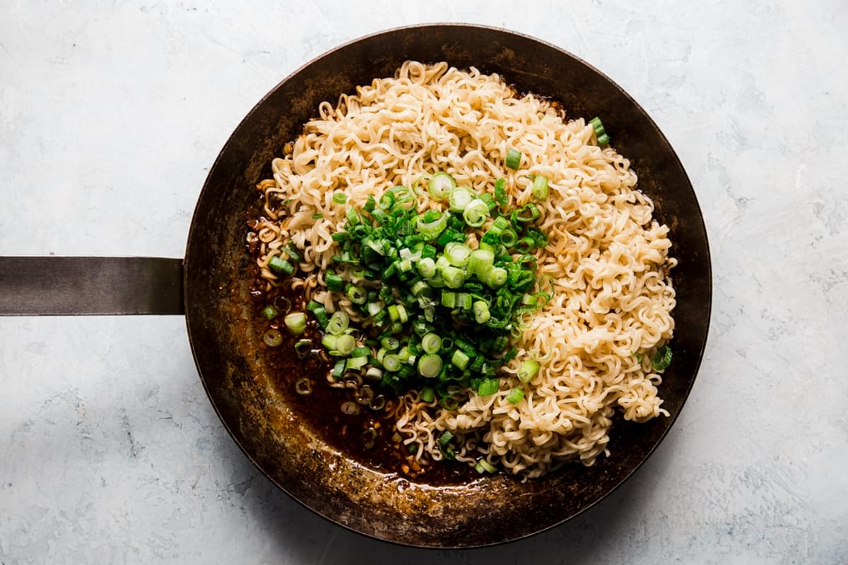 Sesame Garlic Ramen Noodles in a pan with green onions and stir fry sauce.