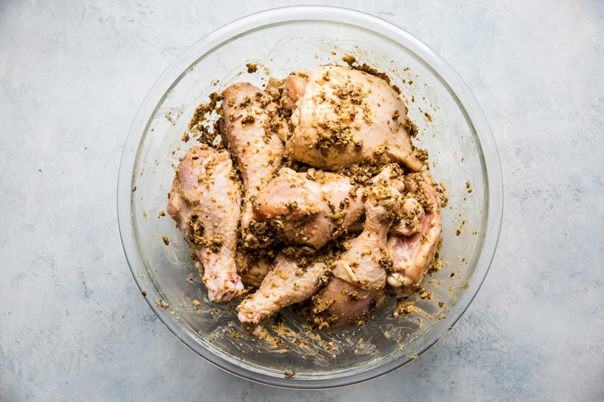 raw chicken legs and thighs in a mixing bowl with a paste marinade of olives, prunes, carpers and garlic