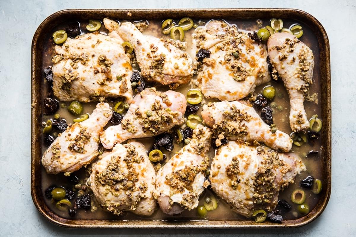 raw chicken marbella on a sheet pan with olives and prunes