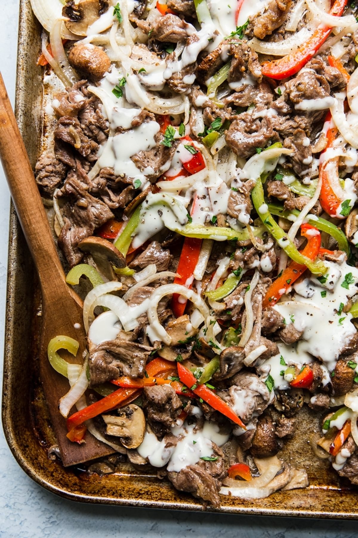 Steak, red and green bell peppers, onions and mushrooms with cheese sauce on a rimmed baking sheet for Philly Cheesesteak