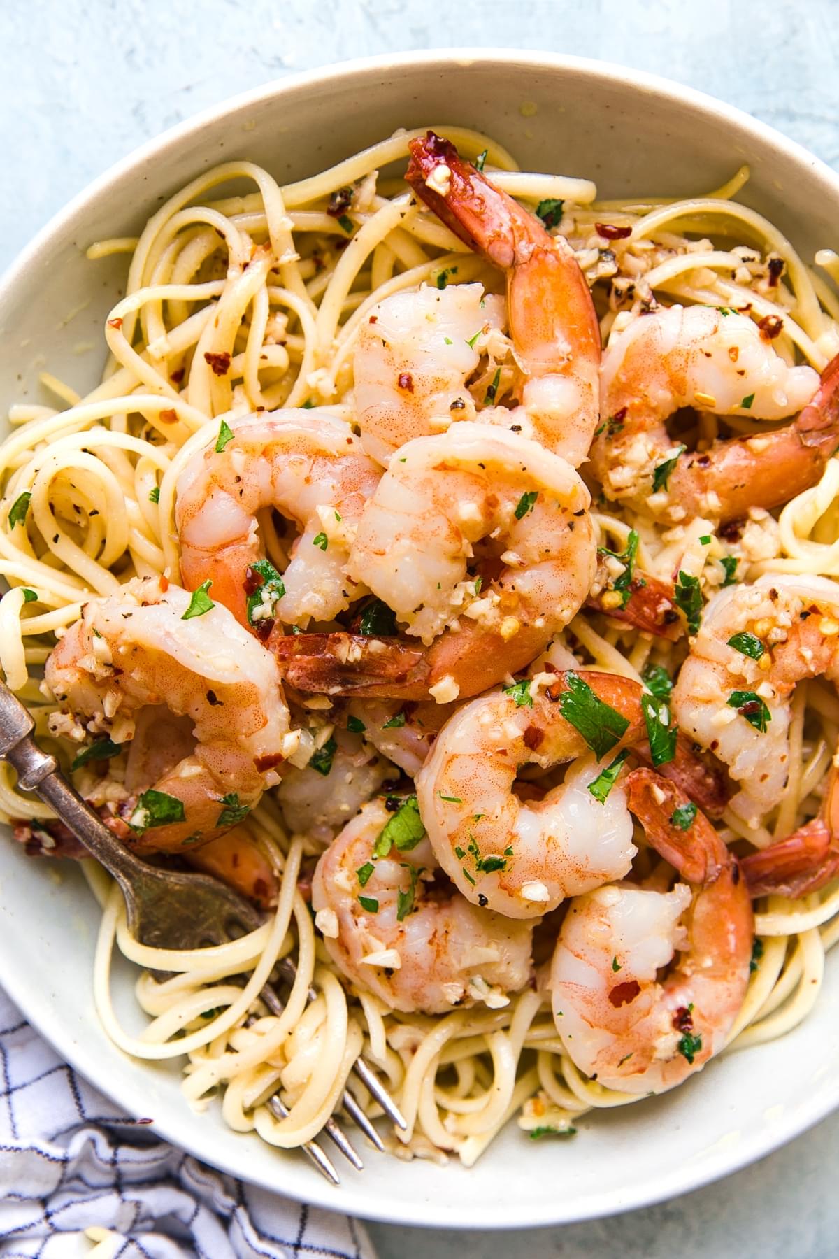 shrimp scampi over pasta in a white bowl topped with red pepper flakes and fresh parsley