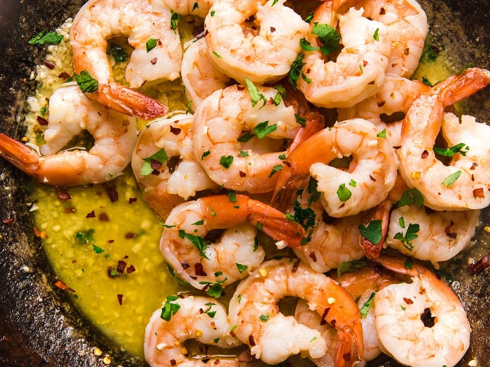 shrimp scampi in a large metal skillet topped with fresh parsley