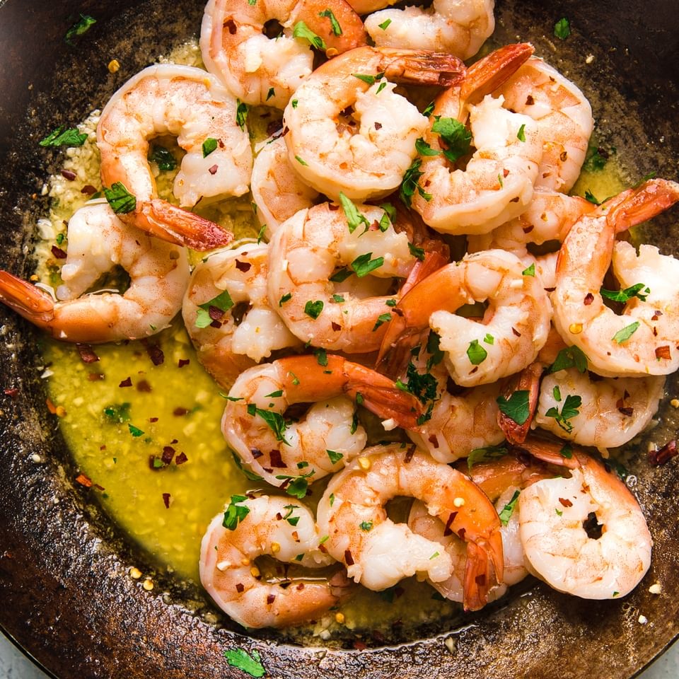 shrimp scampi in a large metal skillet topped with fresh parsley
