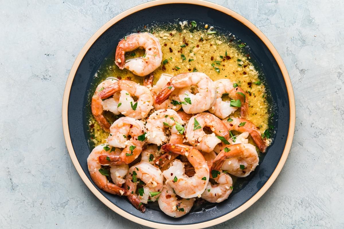 shrimp scampi in a garlic butter sauce on a blue plate topped with fresh parsley