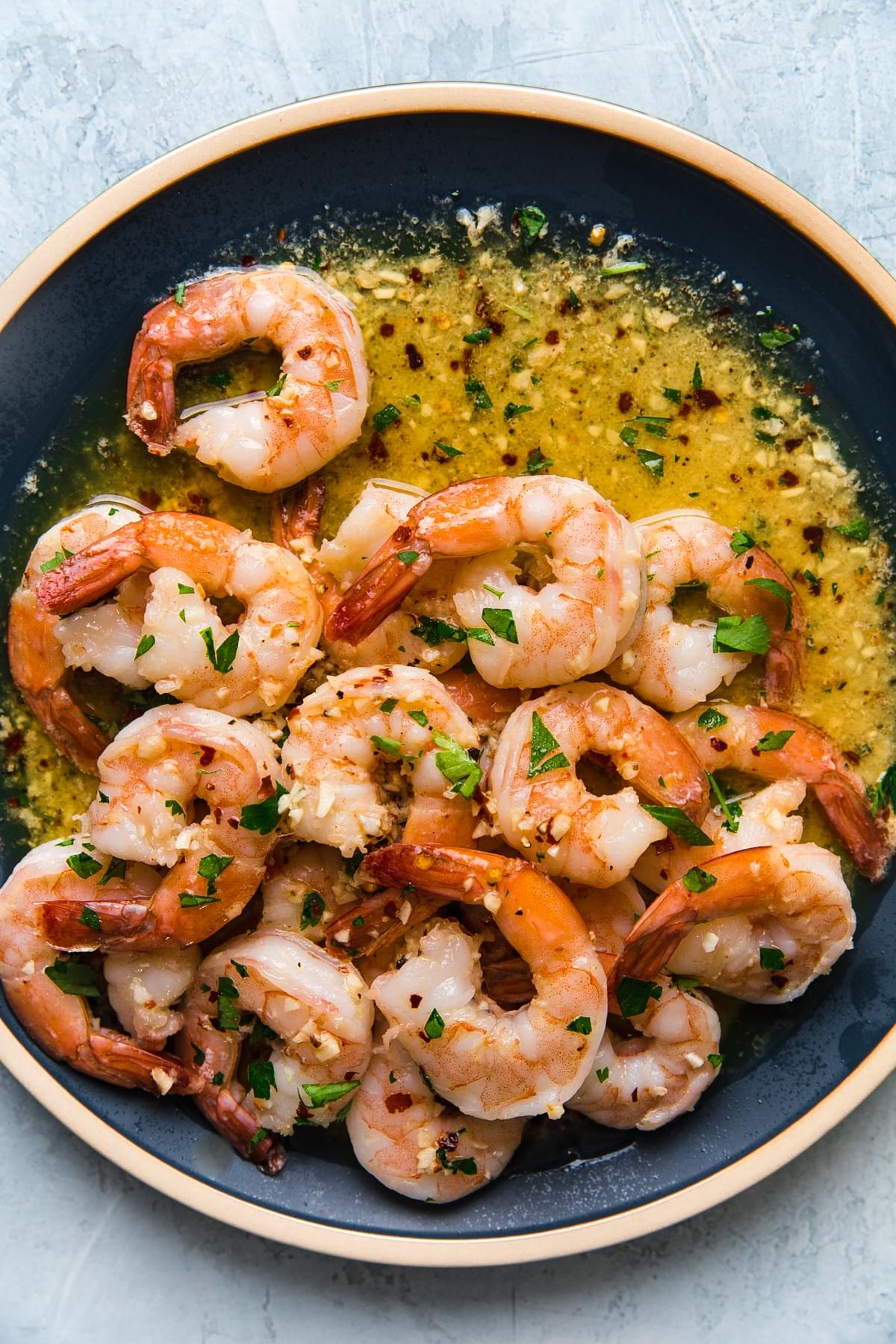 shrimp scampi on a blue ceramic plate topped with fresh parsley