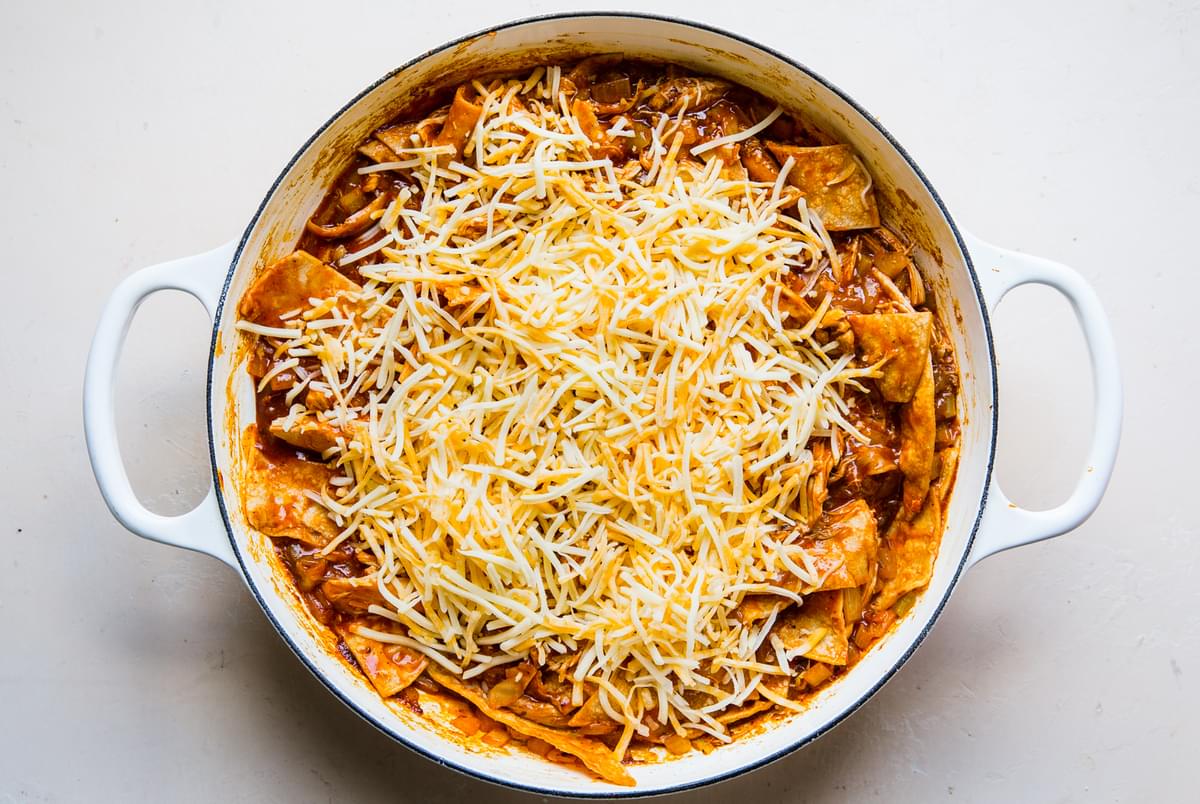 red enchilada sauce mixed with corn tortilla strips and topped with shredded cheese