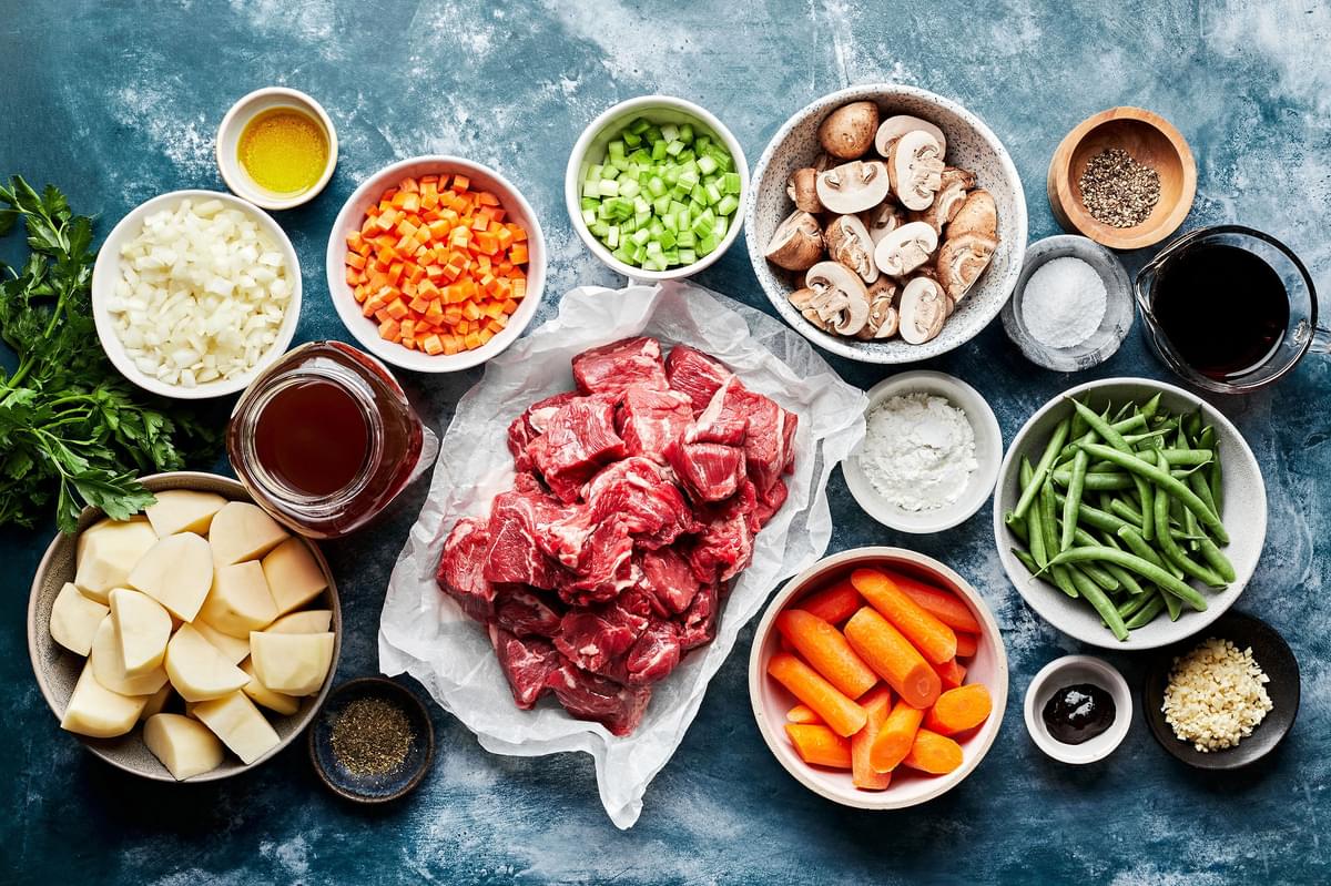 ingredients for slow cooker beef stew in prep bowls: beef, potatoes, vegetables, spices, beef stock and red wine
