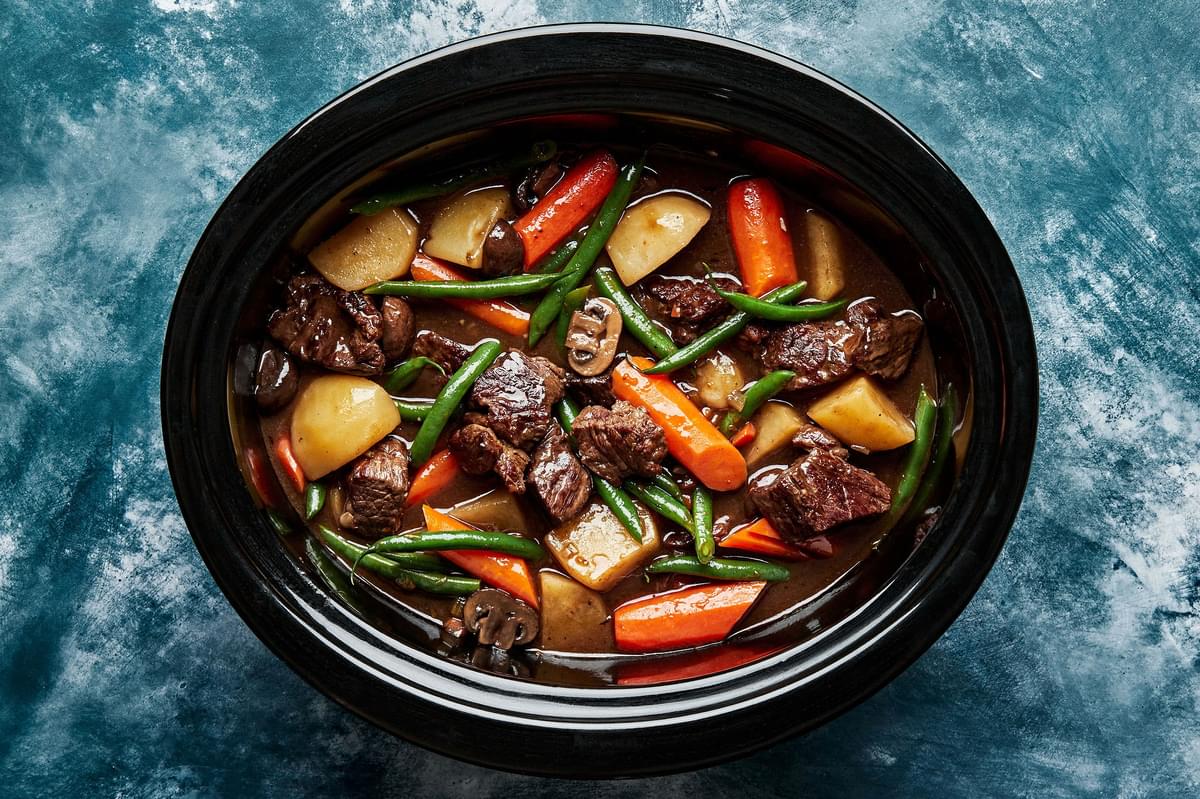 beef stew in a slow cooker made with potatoes, green beans, carrots, onions and celery