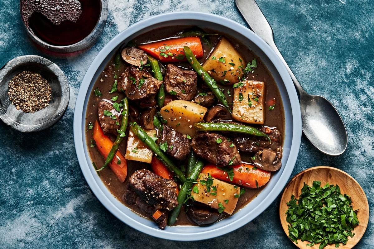 a bowl of slow cooker beef stew made with potatoes, green beans, carrots, onions and celery
