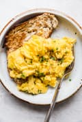 Soft Scrambled Eggs on a plate with chives and toasted bread