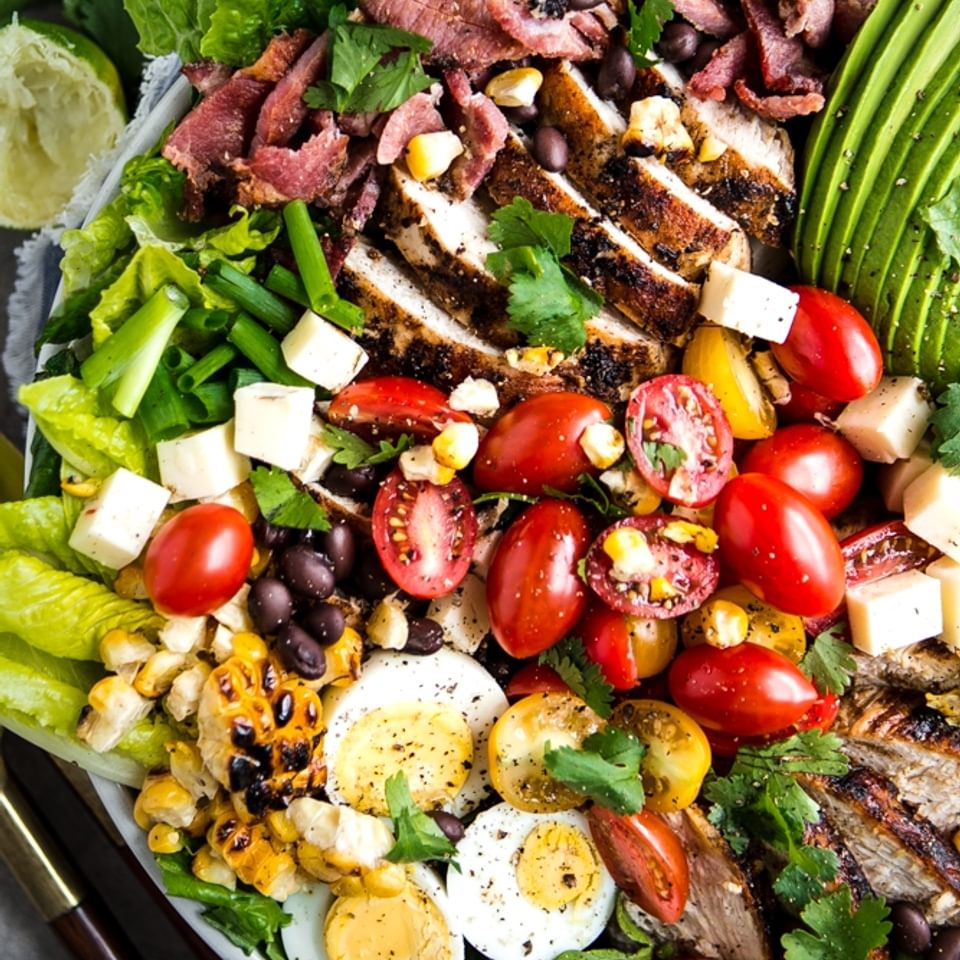 southwest cobb salad with bacon, chipotle dressing, avocado, corn and beans in a bowl