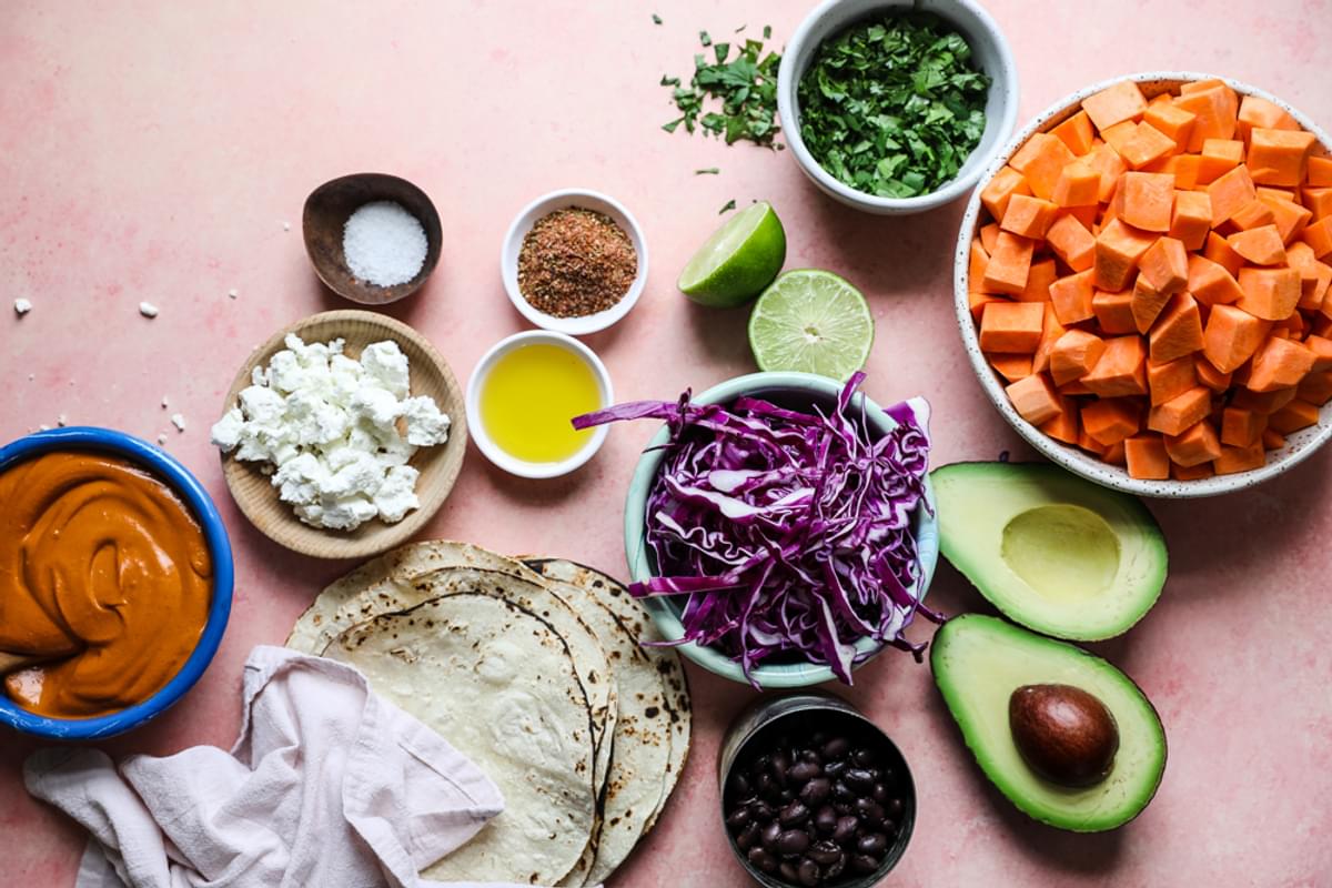 ingredients for sweet potato tacos. red cabbage, black beans, avocado, goat cheese and a bowl of vegan cashew sauce.