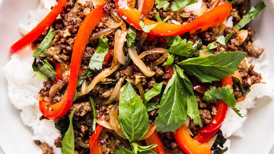 thai basil beef over white rice in a large white bowl