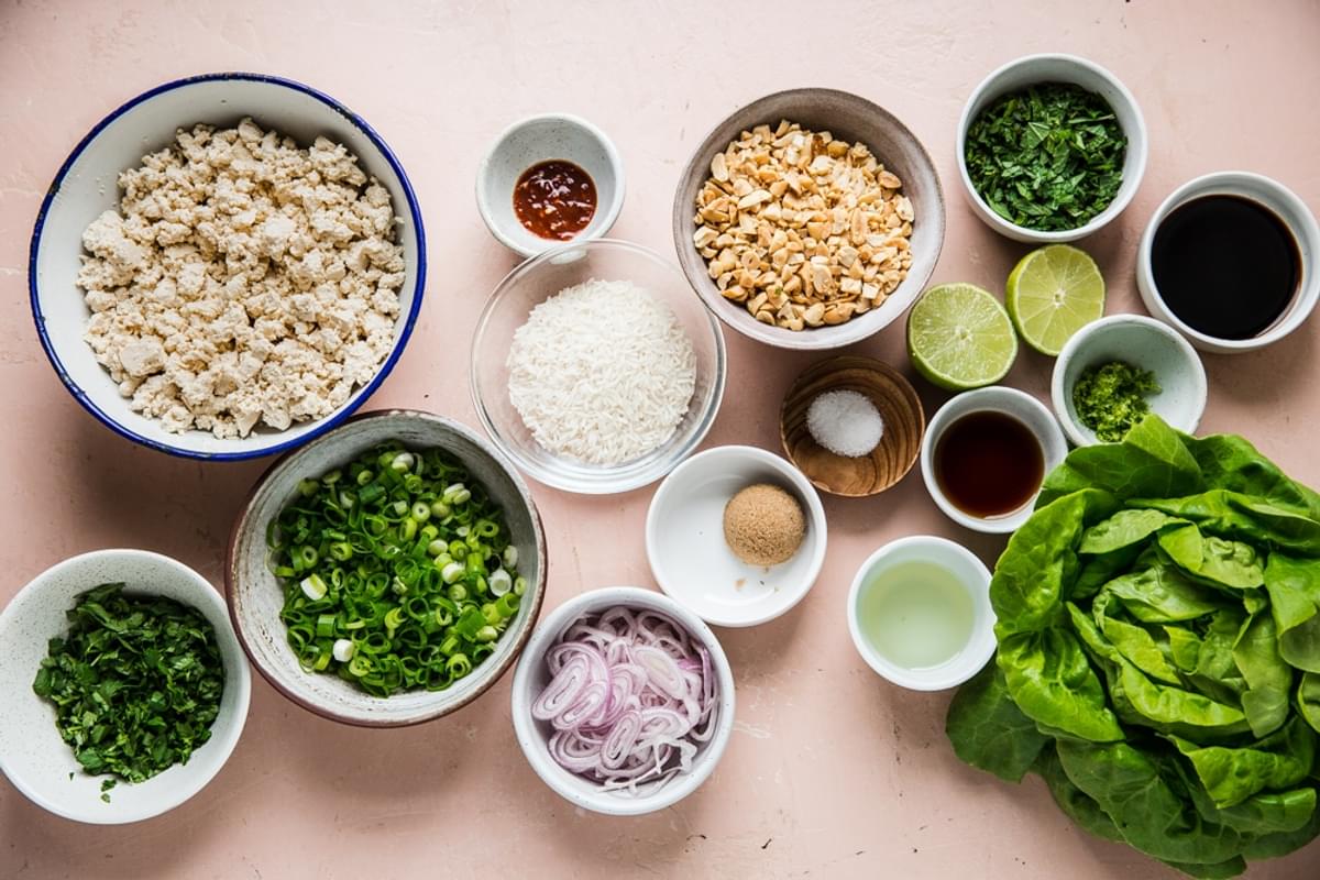 Ingredients for tofu lettuce wraps shown in small bowls including butter lettuce, crumbled tofu, green onions, mint, cilantro