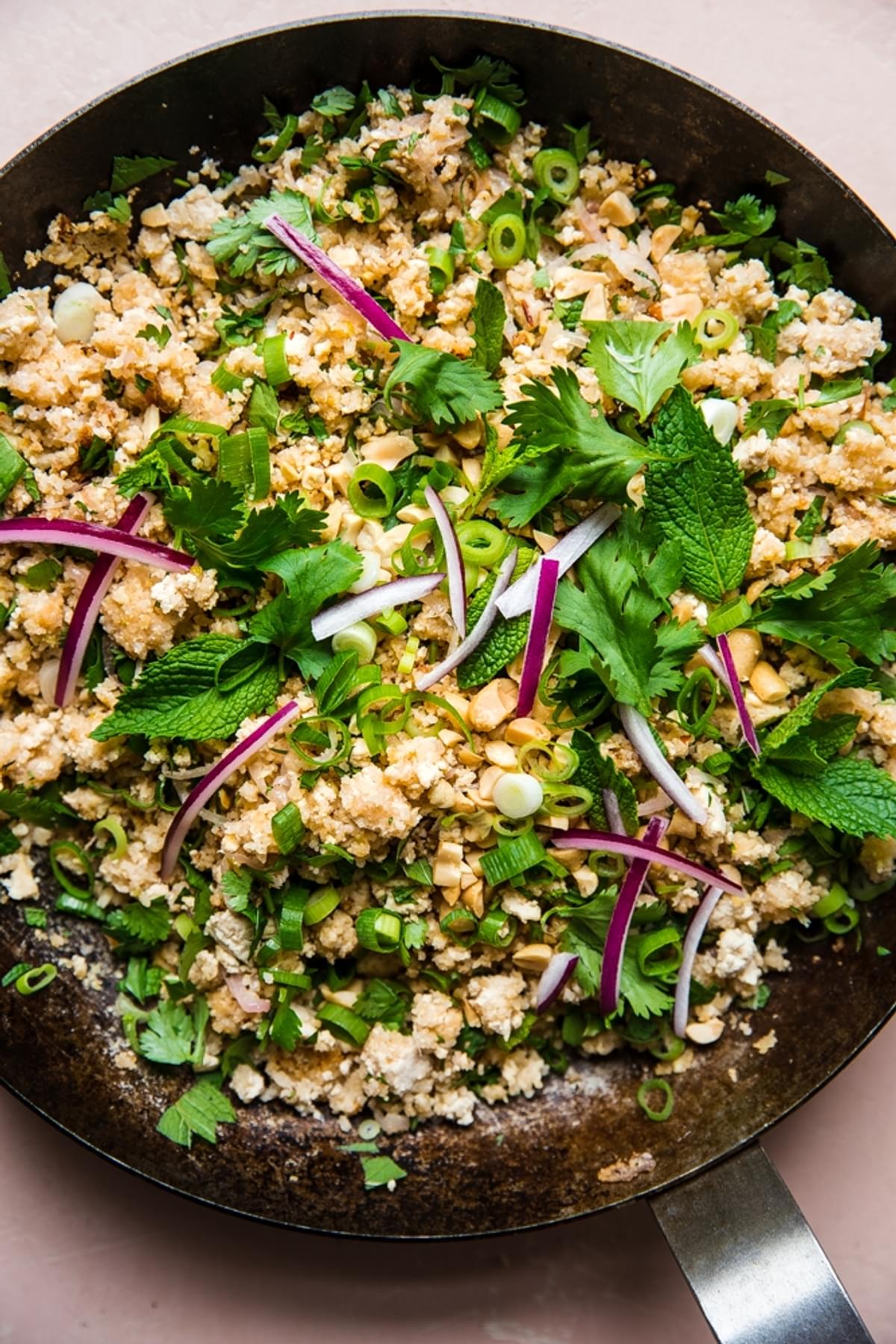 tofu lettuce wrap filling shown in a large skillet and topped with red onions and fresh herbs