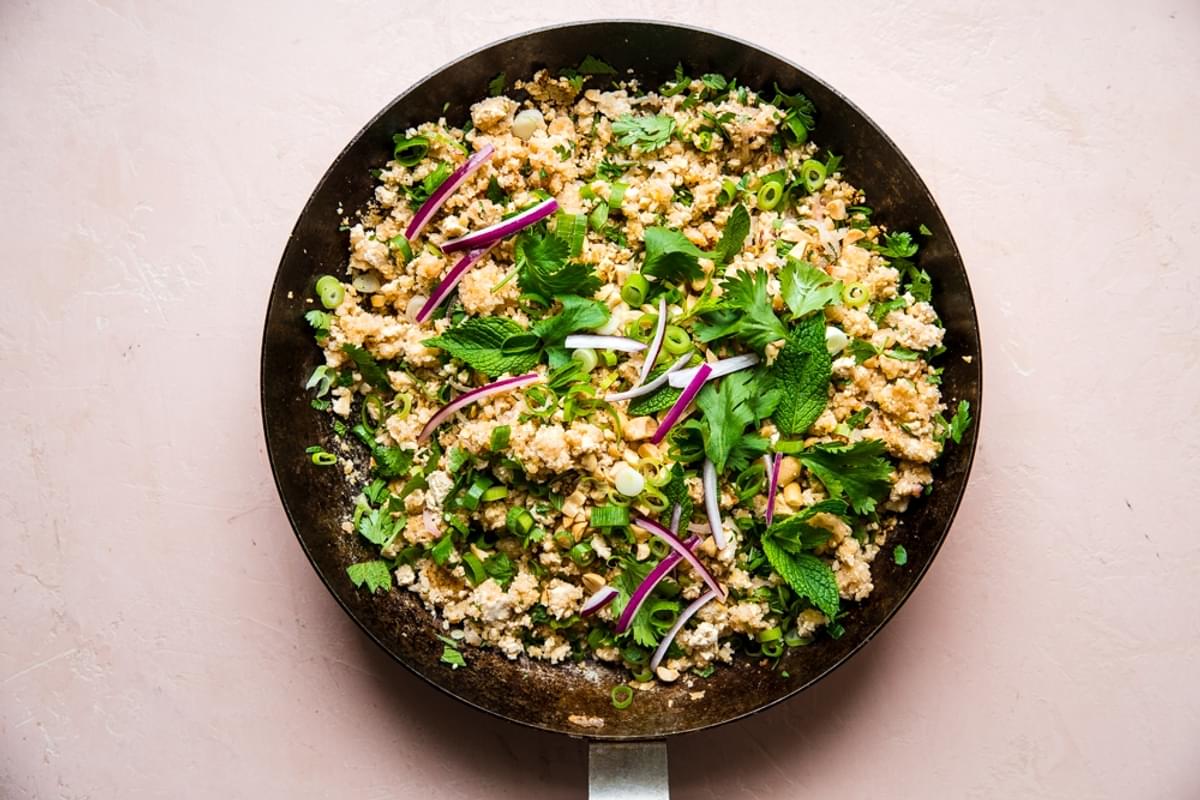 Tofu for lettuce wraps shown in a large metal skillet topped with fresh herbs and red onions