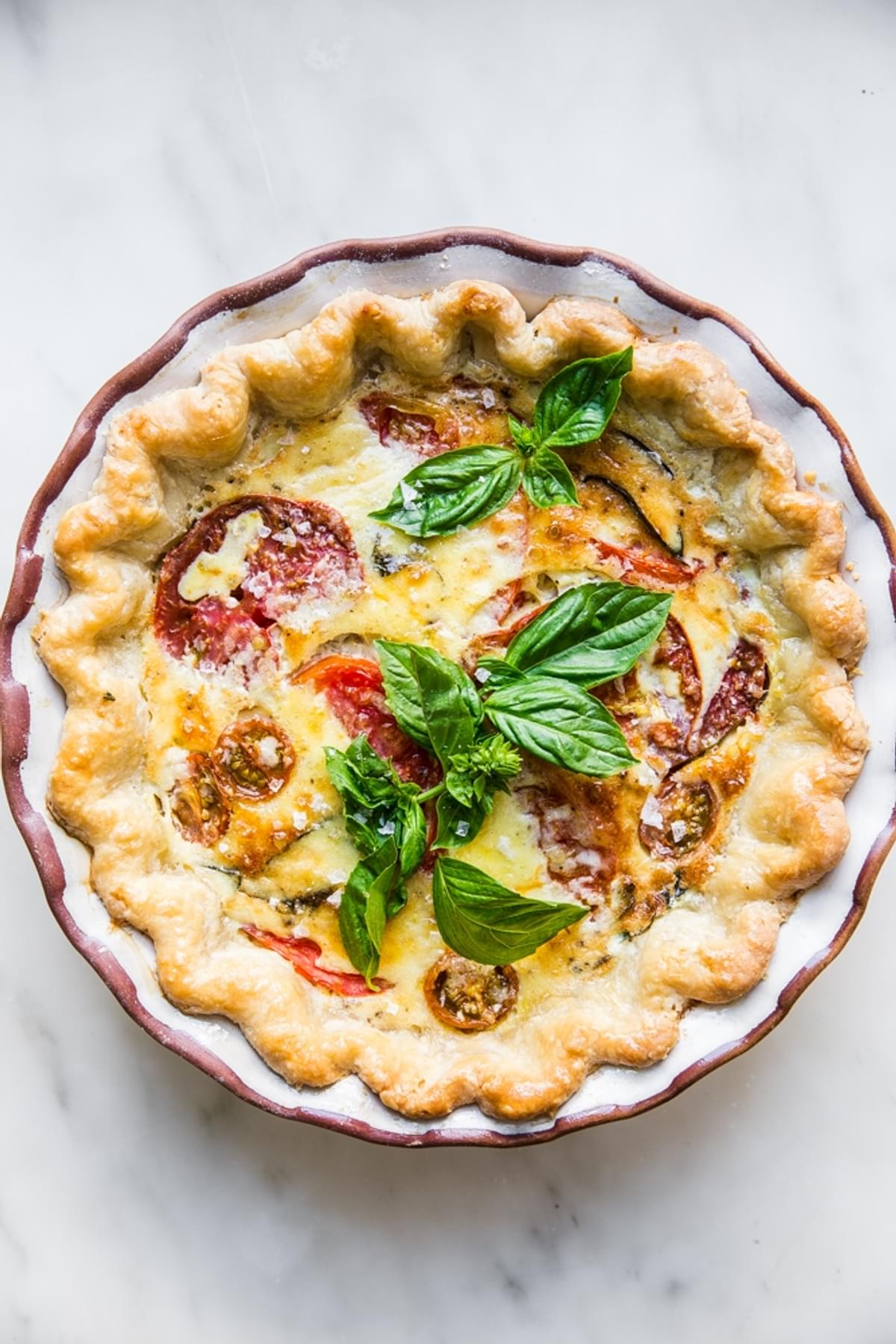 tomato, basil and caramelized onion quiche topped with parmesan in a ceramic pie pan