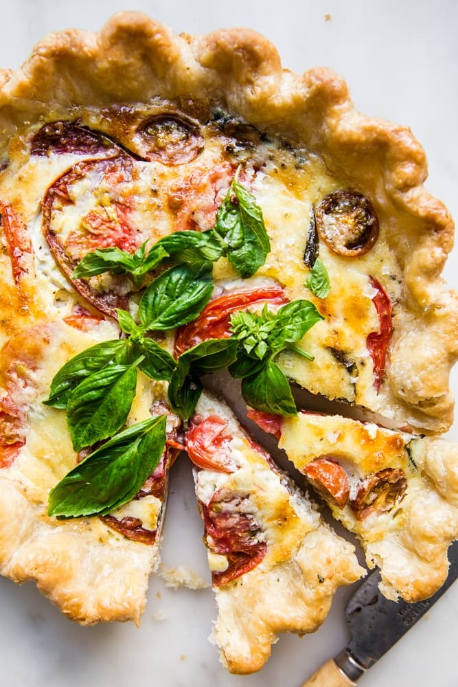 tomato basil and caramelized onion quiche with two slices cut out of it shown with a sharp knife.
