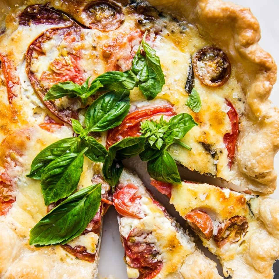 tomato basil and caramelized onion quiche with two slices cut out of it shown with a sharp knife.