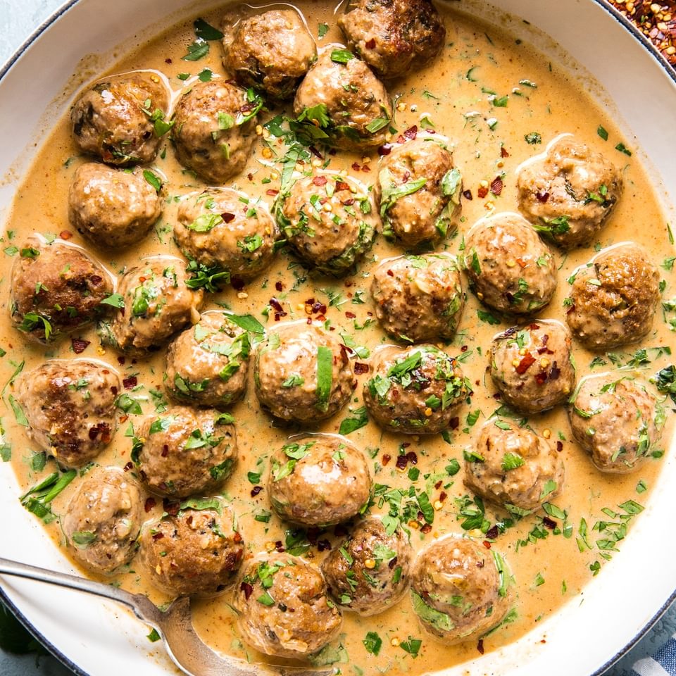 Turkey meatballs in a creamy red curry sauce topped with red pepper flakes and fresh cilantro in a skillet.