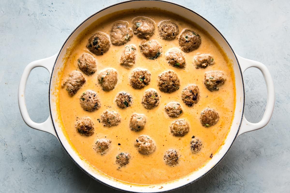 turkey meatballs in a red curry sauce in a large white skillet