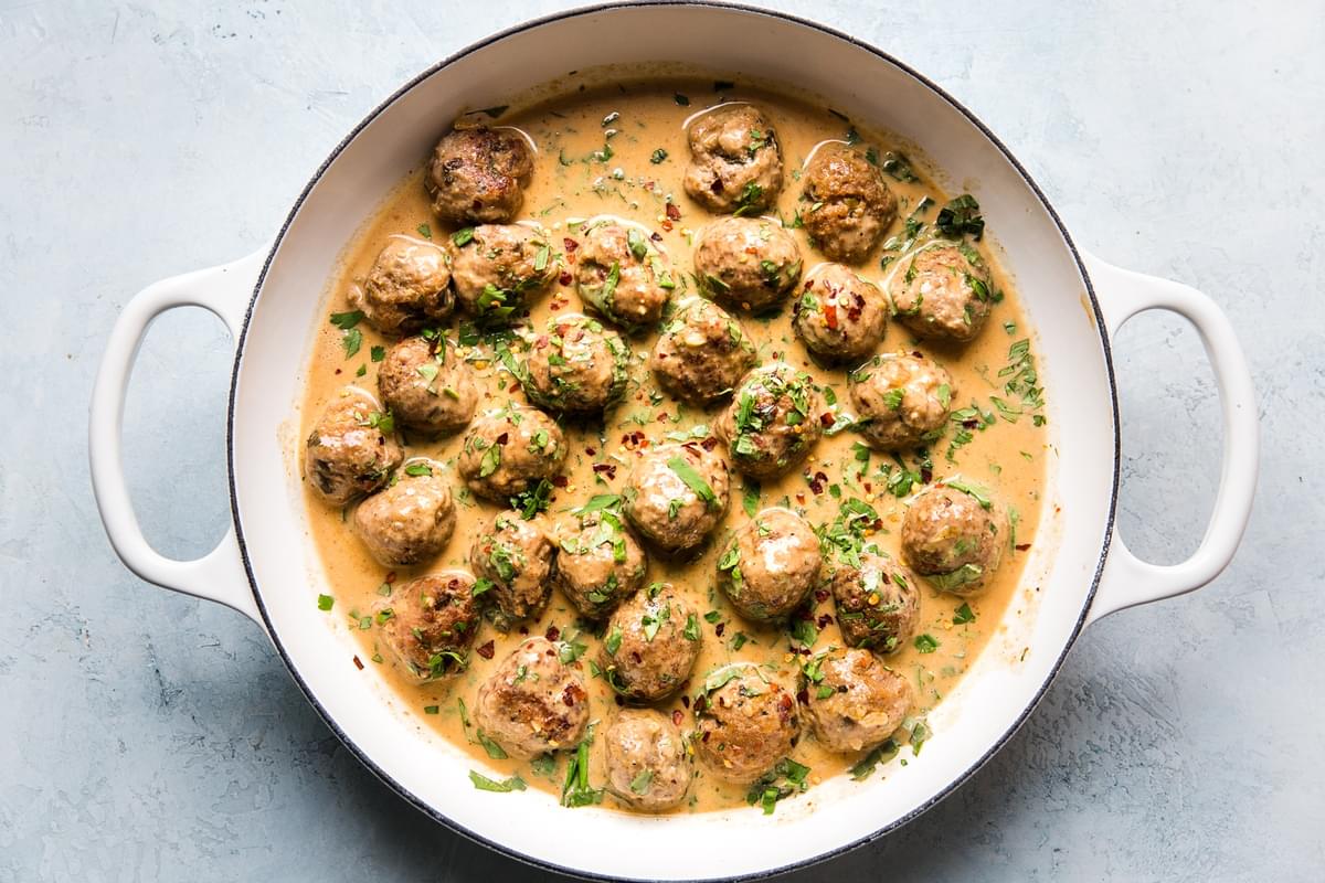 turkey meatballs in a red curry sauce topped with fresh cilantro in a large white skillet