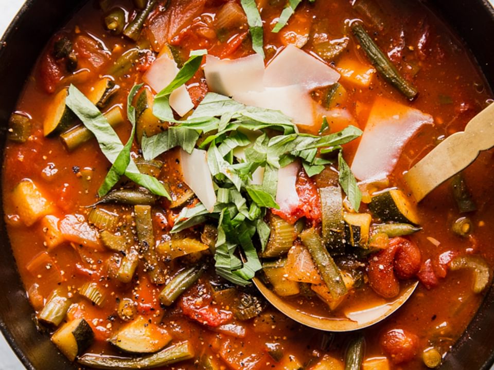 a pot of homemade vegetable soup topped with fresh basil and shaved parmesan