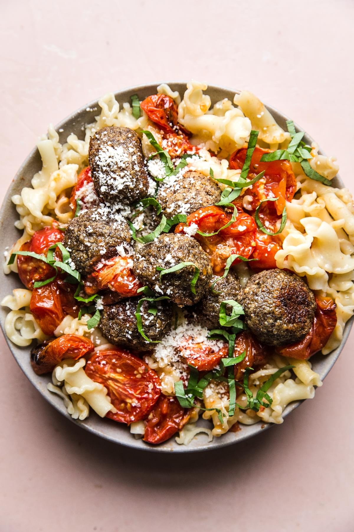 vegetarian meatballs with roasted tomatoes over pasta topped with parmesan cheese and fresh basil