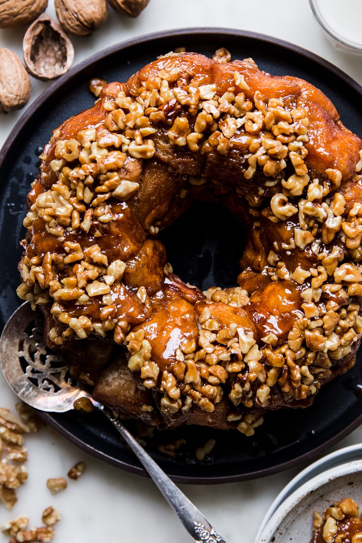 Monkey bread with walnuts and vanilla shown on a black platter with a silver serving spoon