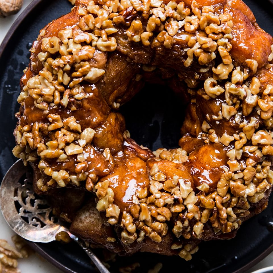 Monkey bread with walnuts and vanilla shown on a black platter with a silver serving spoon