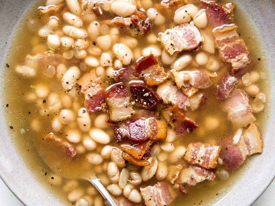 white bean and bacon soup in a bowl with a spoon