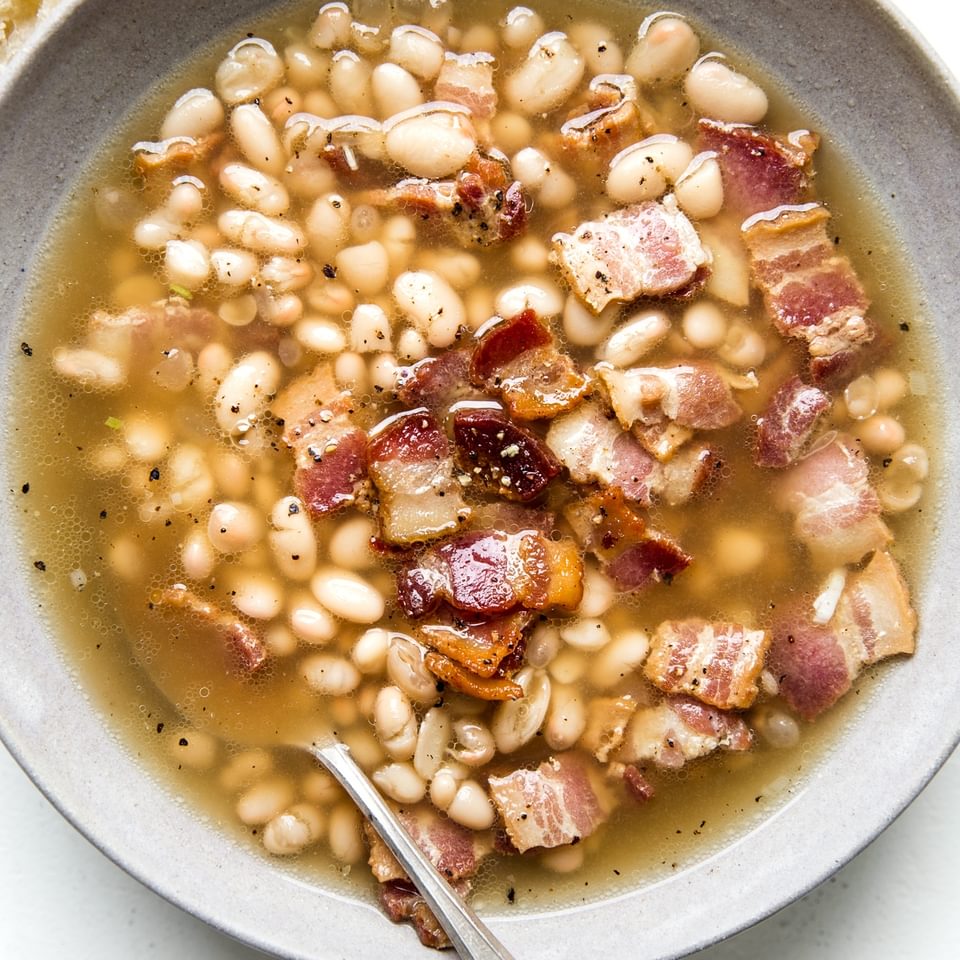 white bean and bacon soup in a bowl with a spoon