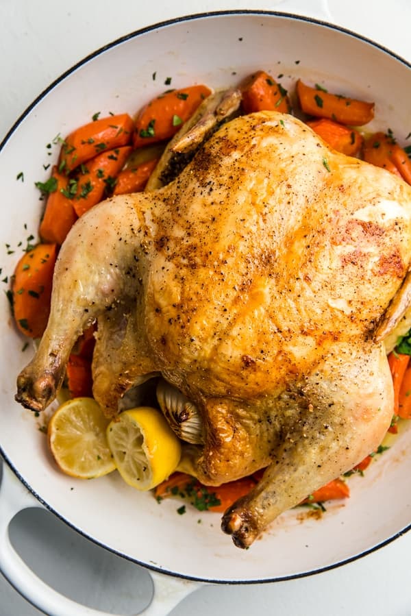 whole roasted chicken over a bed of carrots shown in a large white braiser