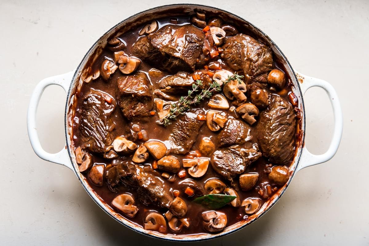 beef and mushrooms with red wine sauce in a white braiser