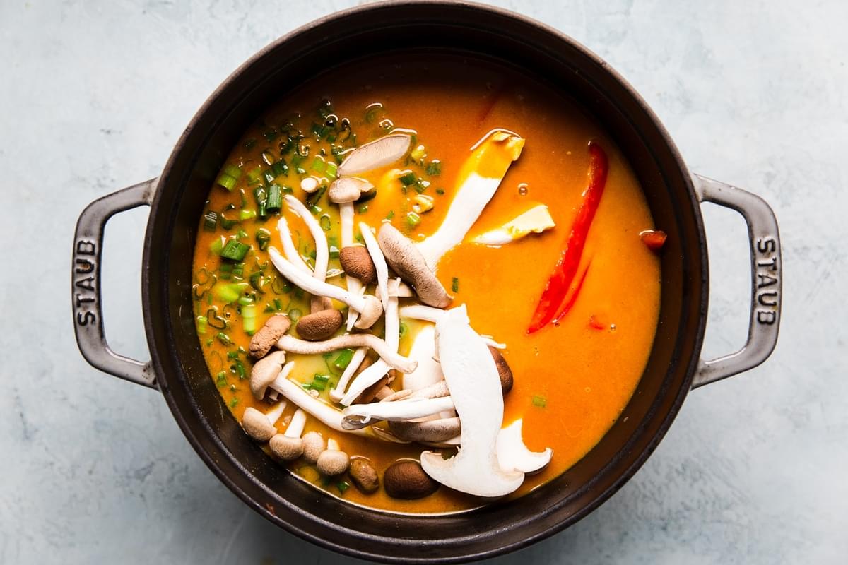 Coconut curry doodle ramen with mushrooms and red bell peppers in a soup pot. Vegan curry vegetarian curry.