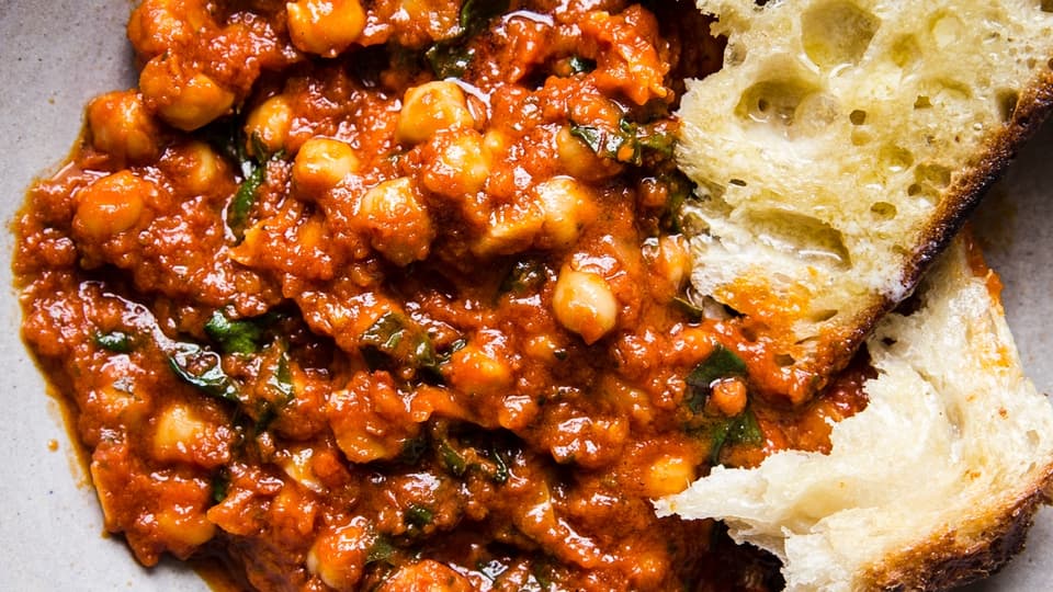 braised chickpeas in a tomato sauce with chard shown in a ceramic bowl with crusty bread