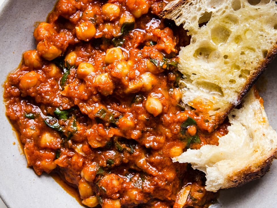 braised chickpeas in a tomato sauce with chard shown in a ceramic bowl with crusty bread