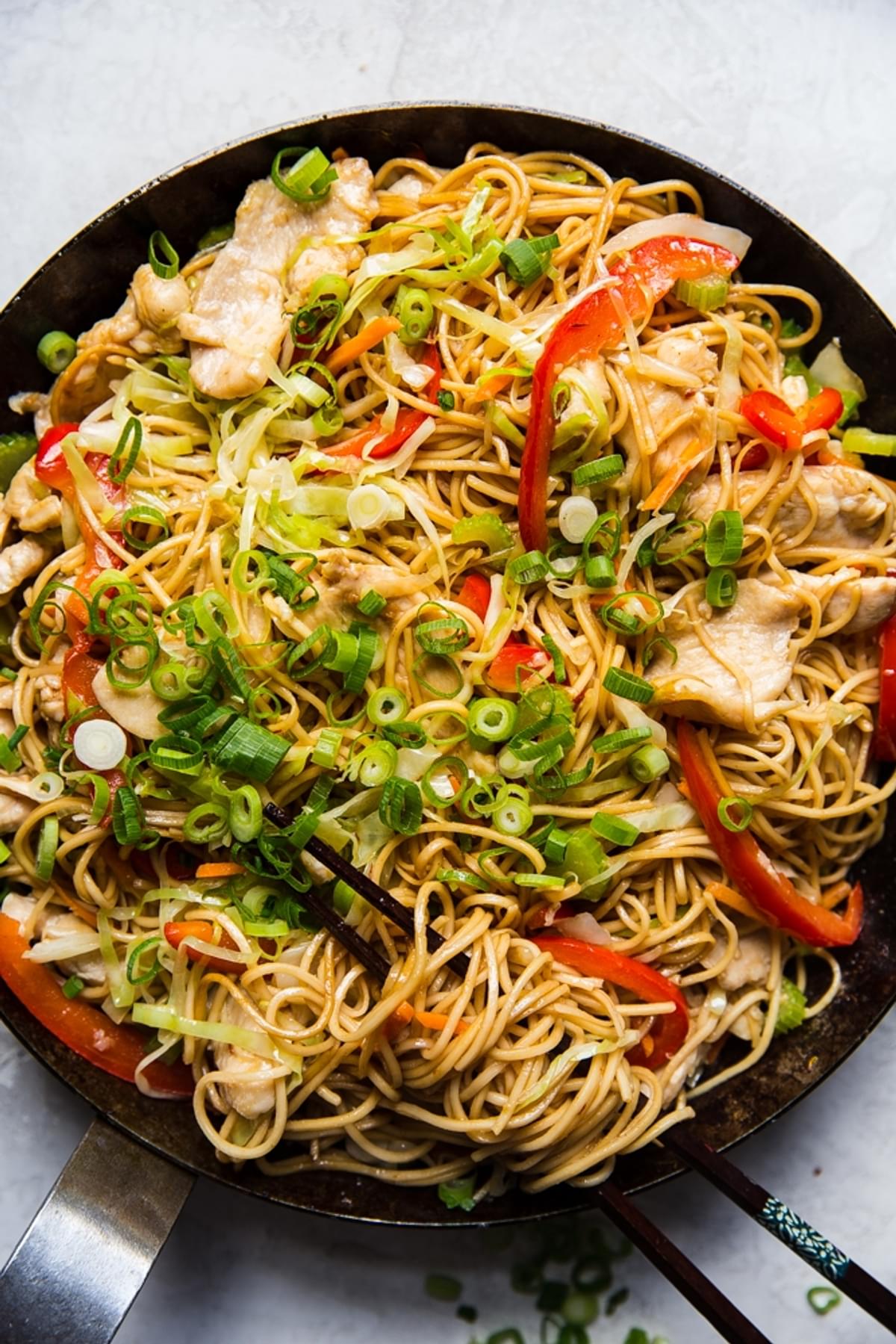 homemade chicken chow mein with bell peppers, celery, carrots and a sauce in a skillet