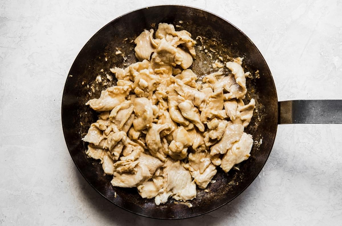 poached chicken pieces and garlic cooking in a large skillet