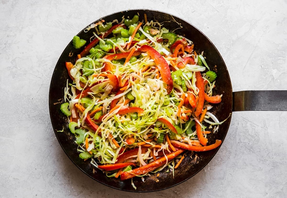 shredded cabbage, sliced bell peppers, chopped celery, shaved carrots, garlic and ginger being cooked in a large skillet