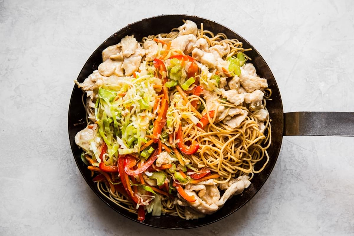 chicken, chow mein noodles and stir fried veggies being tossed in sauce in a skillet
