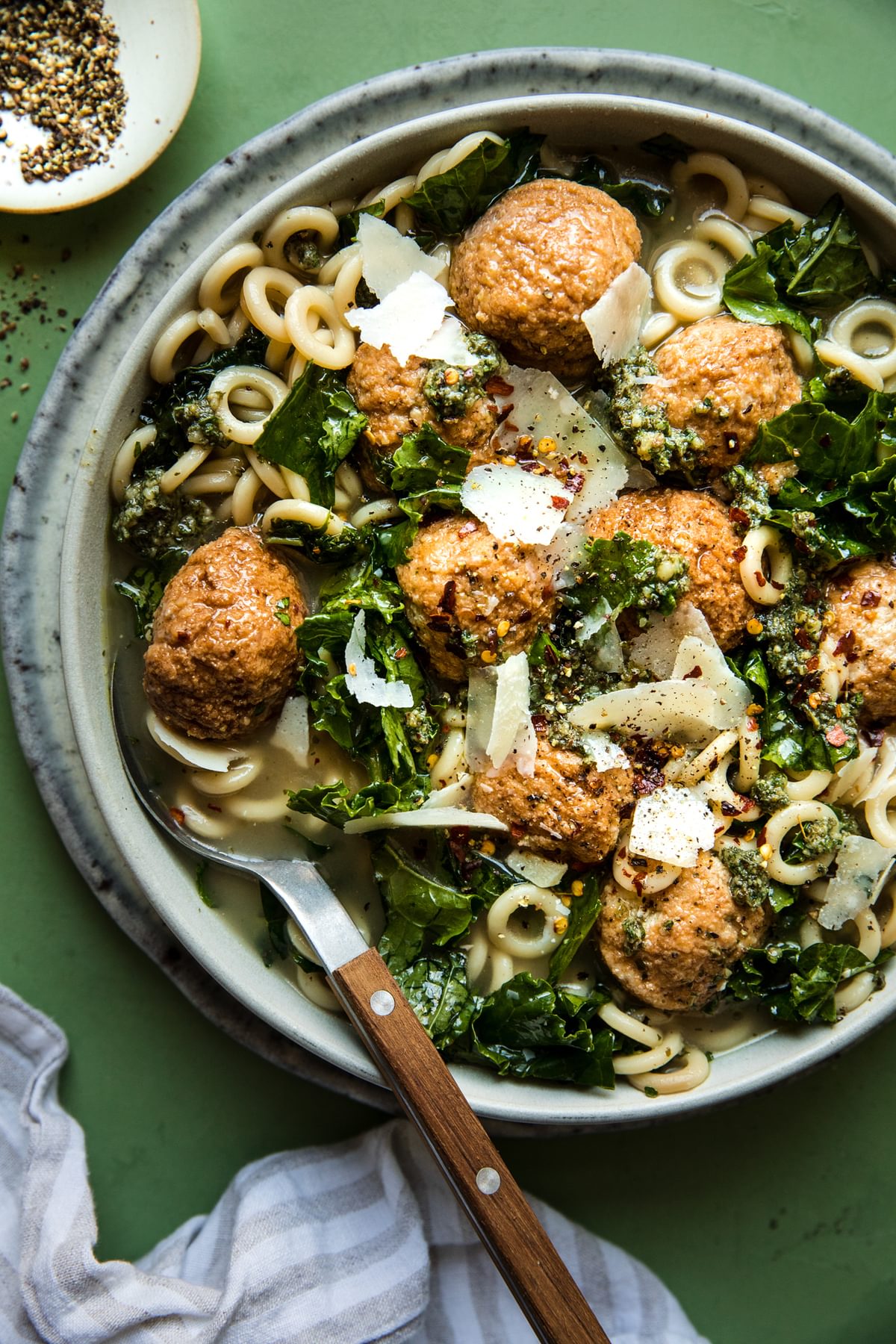 a bowl of chicken meatball soup with kale and parmesan in a bowl with a spoon
