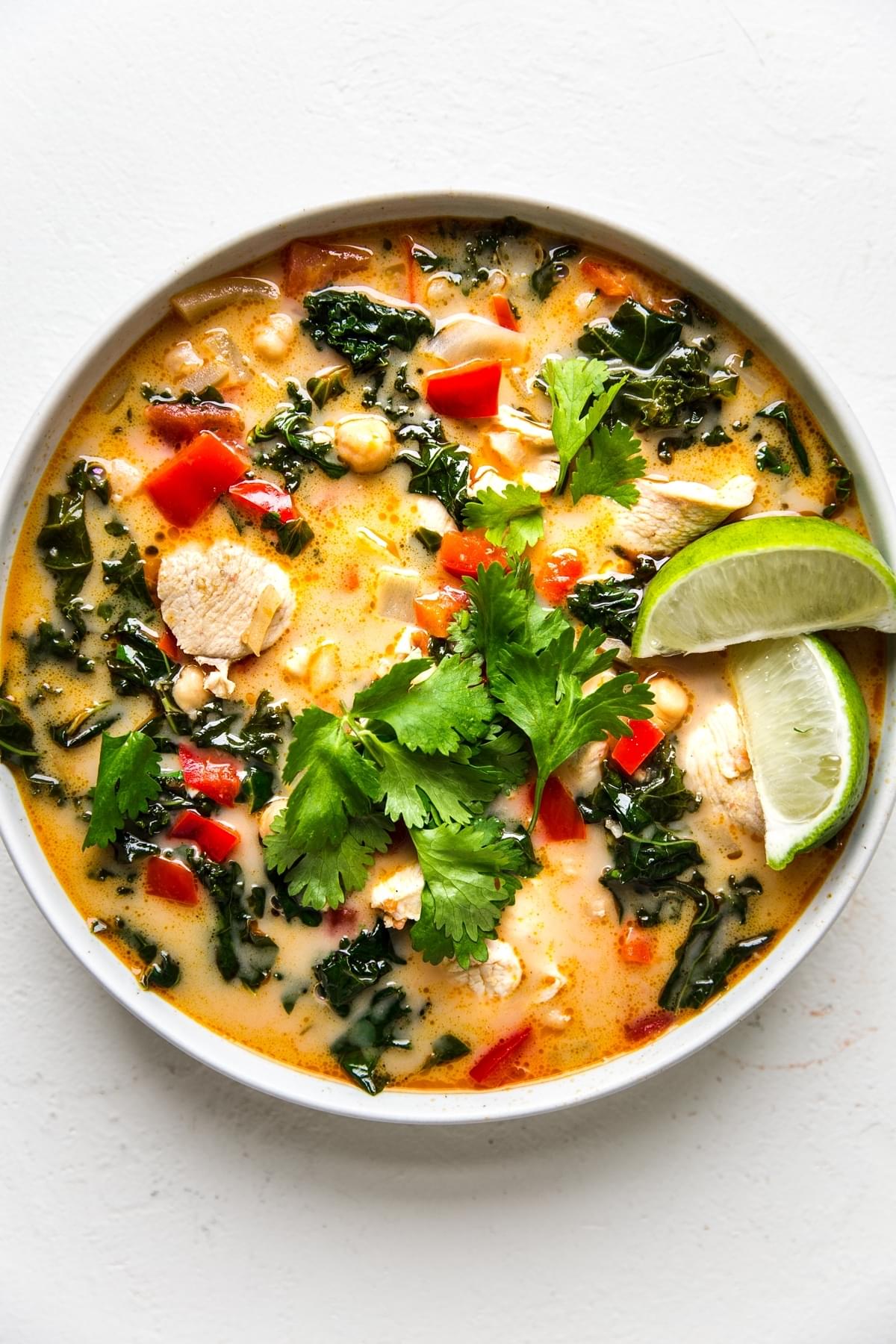 coconut curry soup in a white bowl with peppers, kale, chicken, fresh cilantro and chickpeas