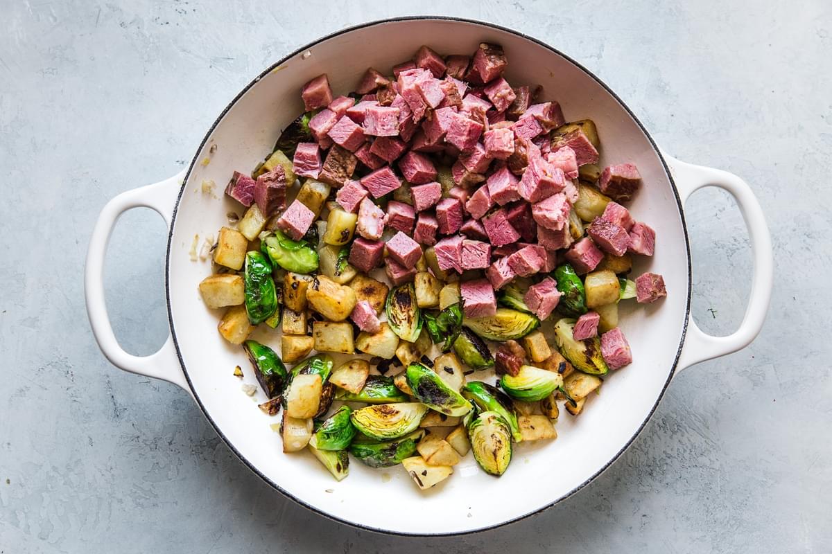 fried potatoes, brussel sprouts and corned beef being cooked in a skillet