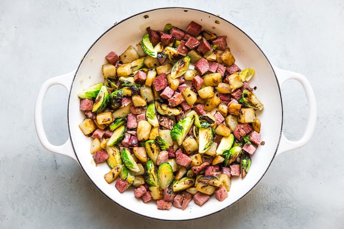 potato, brussel sprouts and corned beef fried in a white skillet