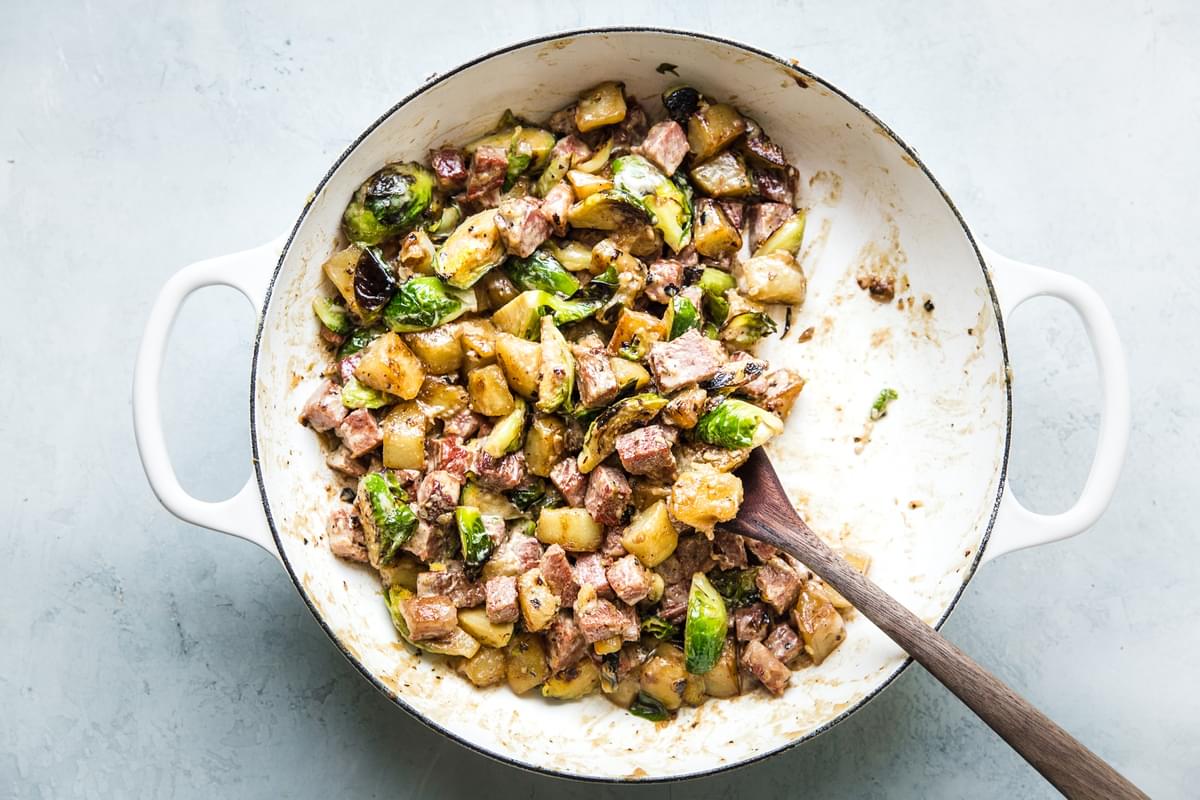 corned beef hash cooking in a pan with potatoes, shallots, brussels sprouts, cream, worcestershire and spices