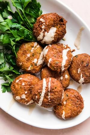 a platter of homemade falafel drizzled with tahini sauce and served with parsley