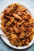 homemade spaghetti sauce tossed with pasta and sausage on a white platter with serving spoon