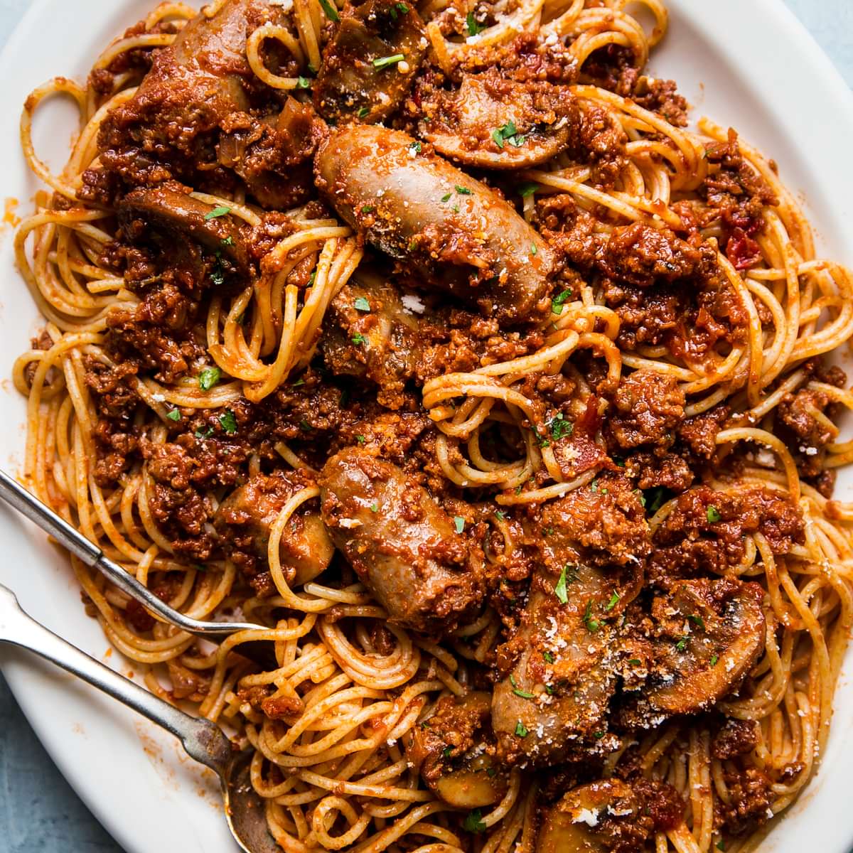 homemade spaghetti sauce tossed with pasta and sausage on a white platter with serving spoon