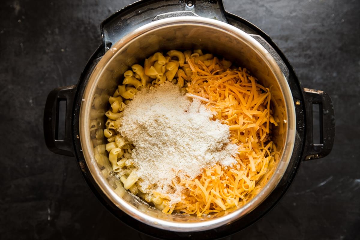 cooked macaroni noodles in an instant pot with shredded cheddar cheese and parmesan